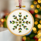 Embroidered snowflake ornament in a wooden hoop with blurred Christmas lights in the background
