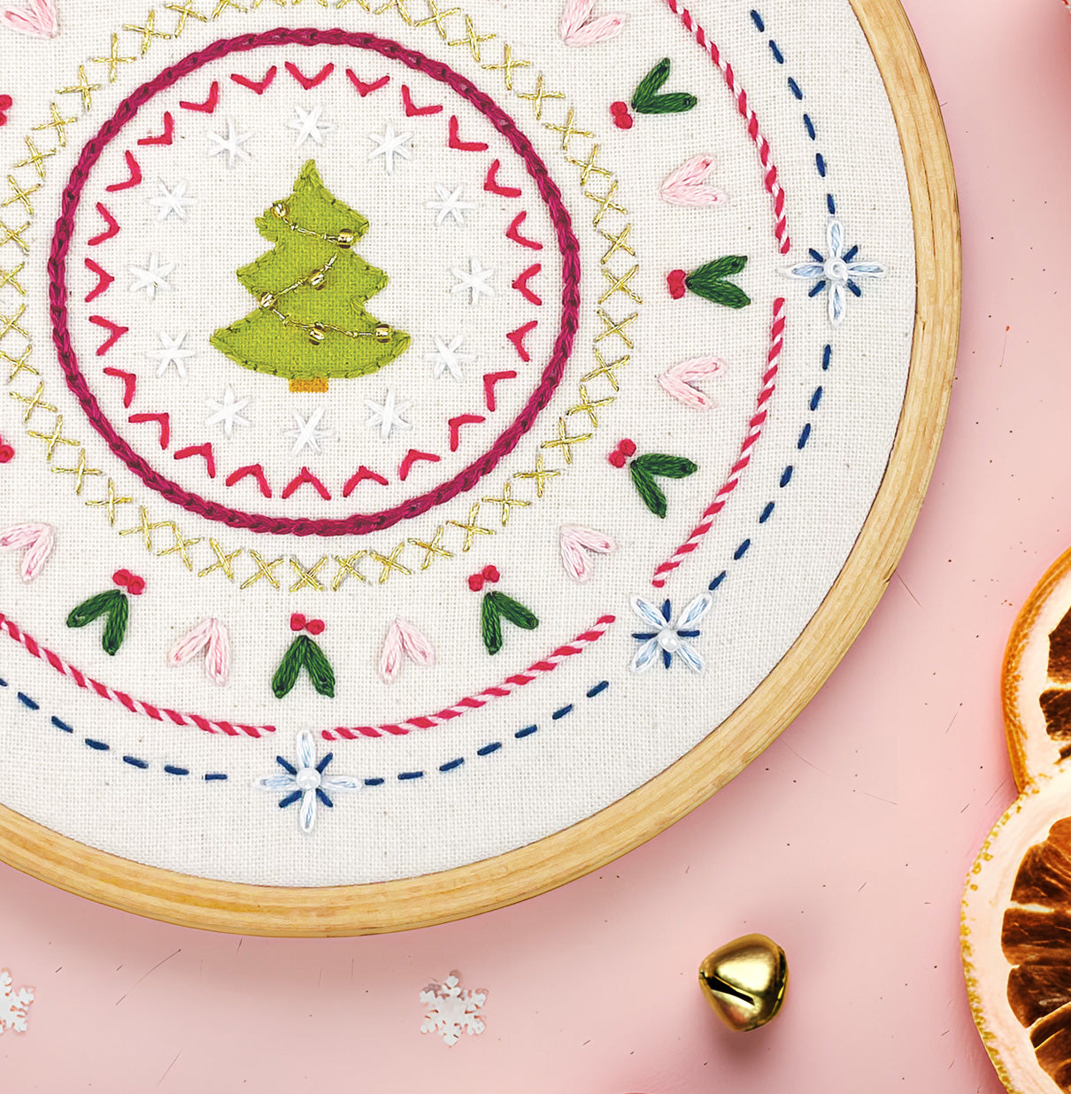 Embroidery hoop with Christmas-themed stitching on a pink background