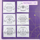 Patterned sweater designs on a grid with measurements on a purple cutting mat.