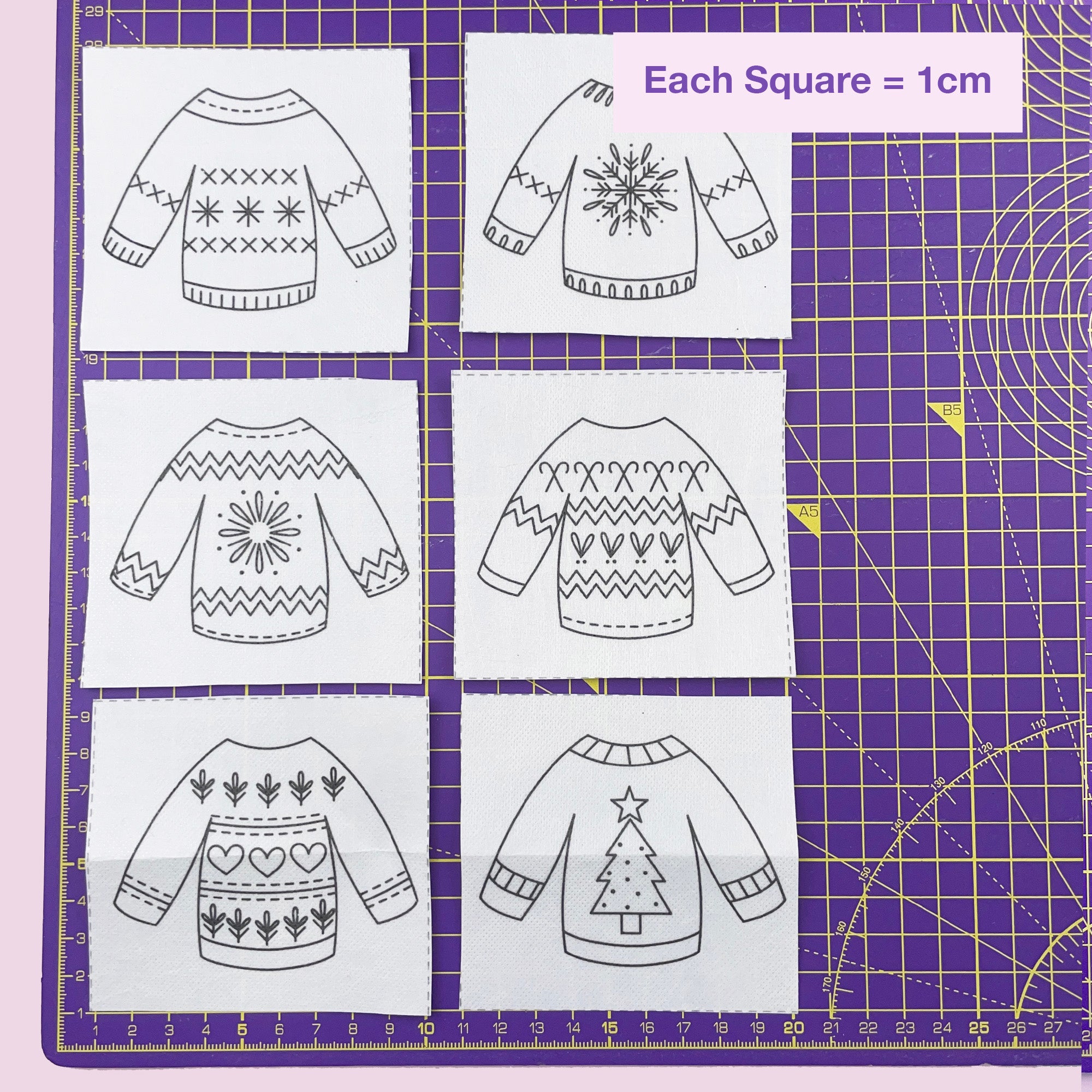 Patterned sweater designs on a grid with measurements on a purple cutting mat.