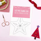 A flat-lay of an iron-on embroidery pattern sheet from Lazy May Sewing Club, featuring a star-shaped outline. The sheet has a pink header label and is wrapped in clear plastic.