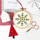 Embroidery hoop with a colorful snowflake design on a white surface with sewing tools.
