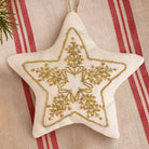 A star-shaped fabric Christmas ornament with a gold embroidered snowflake design, resting on a red and beige striped textile background.