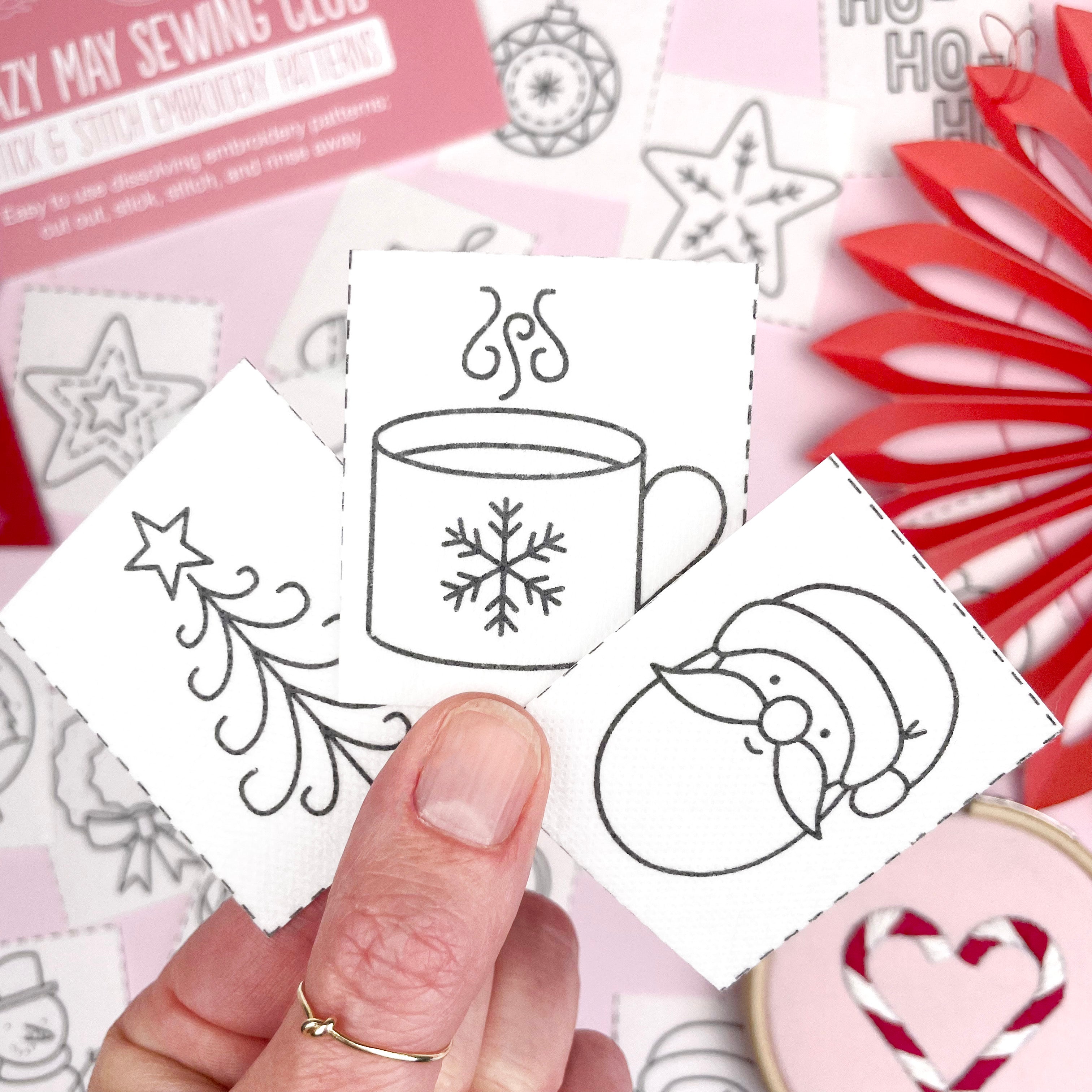 Hand holding a card with black line art designs of a cup, snowflake, and penguin on a pink background.