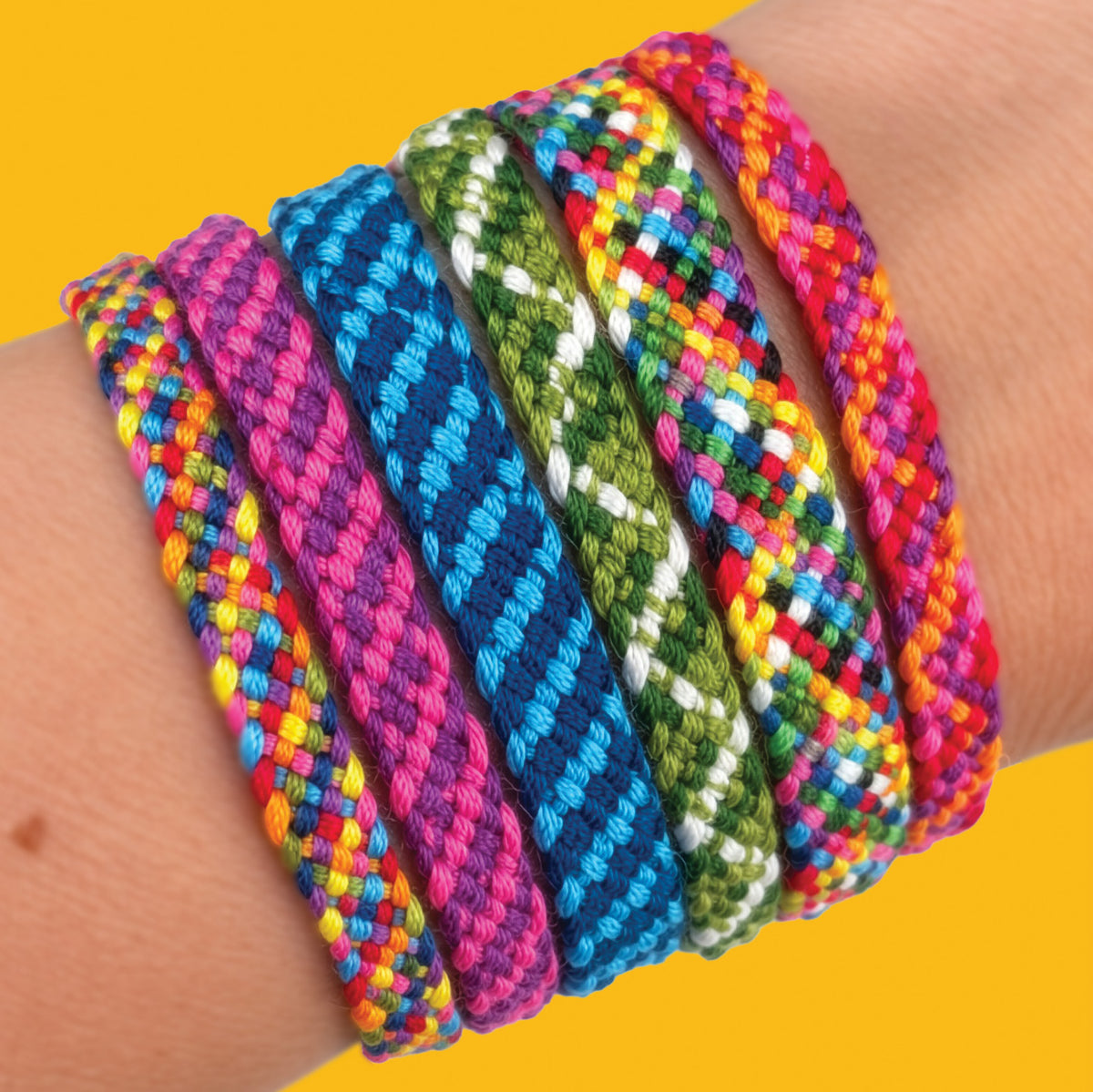 A close-up of a person's wrist wearing six colorful braided friendship bracelets in various patterns, set against a solid yellow background.