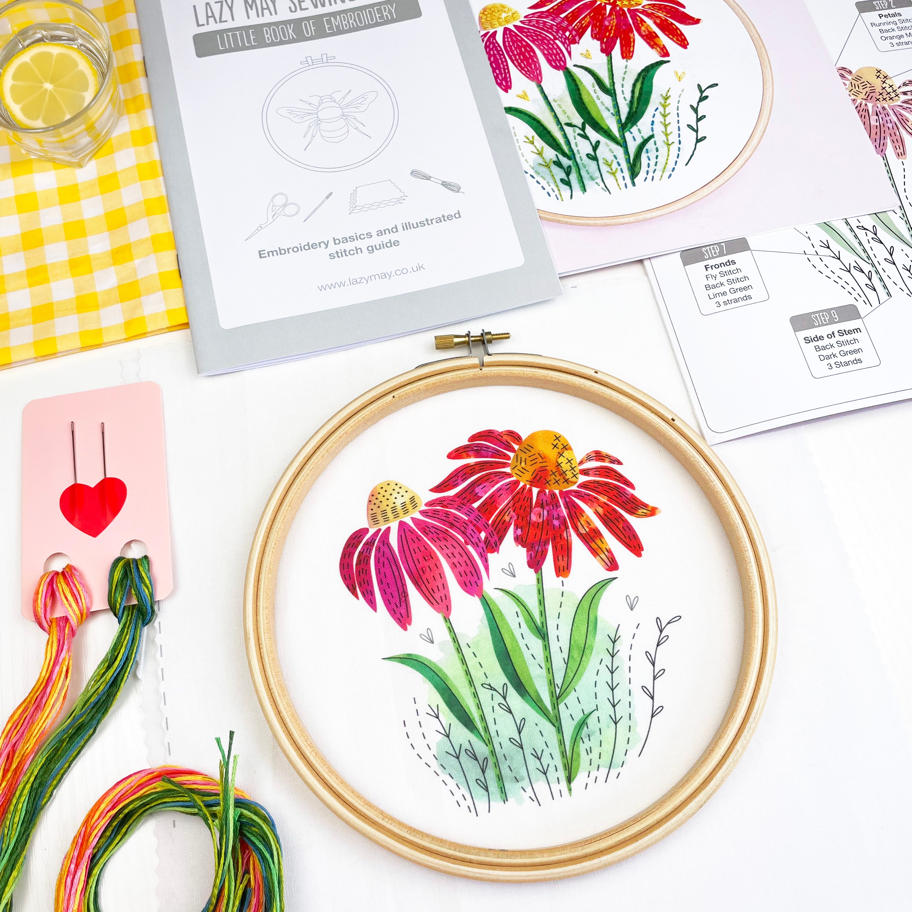 Embroidery hoop with floral coneflower design on a table with embroidery threads and patterns.