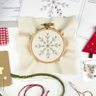 Embroidery hoop with snowflake design on a white fabric background, surrounded by embroidery tools and materials.