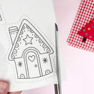 Gingerbread house embroidery pattern with a star and heart design on a white card, held by a hand.