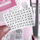 Hand holding embroidery pattern with black X stitches being cut near Slow Stitching Textures: Stick and Stitch Embroidery Patterns packaging