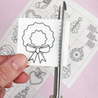 Hand holding a small white card with a black bow design, scissors on a patterned background
