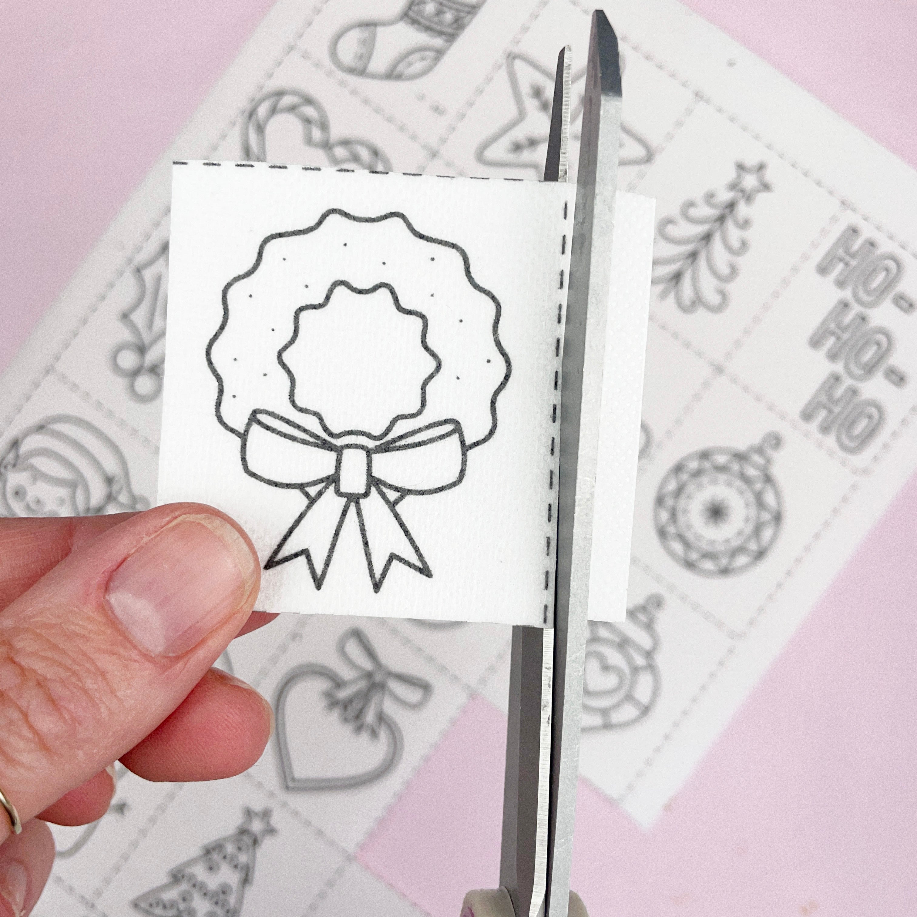 Hand holding a small white card with a black bow design, scissors on a patterned background