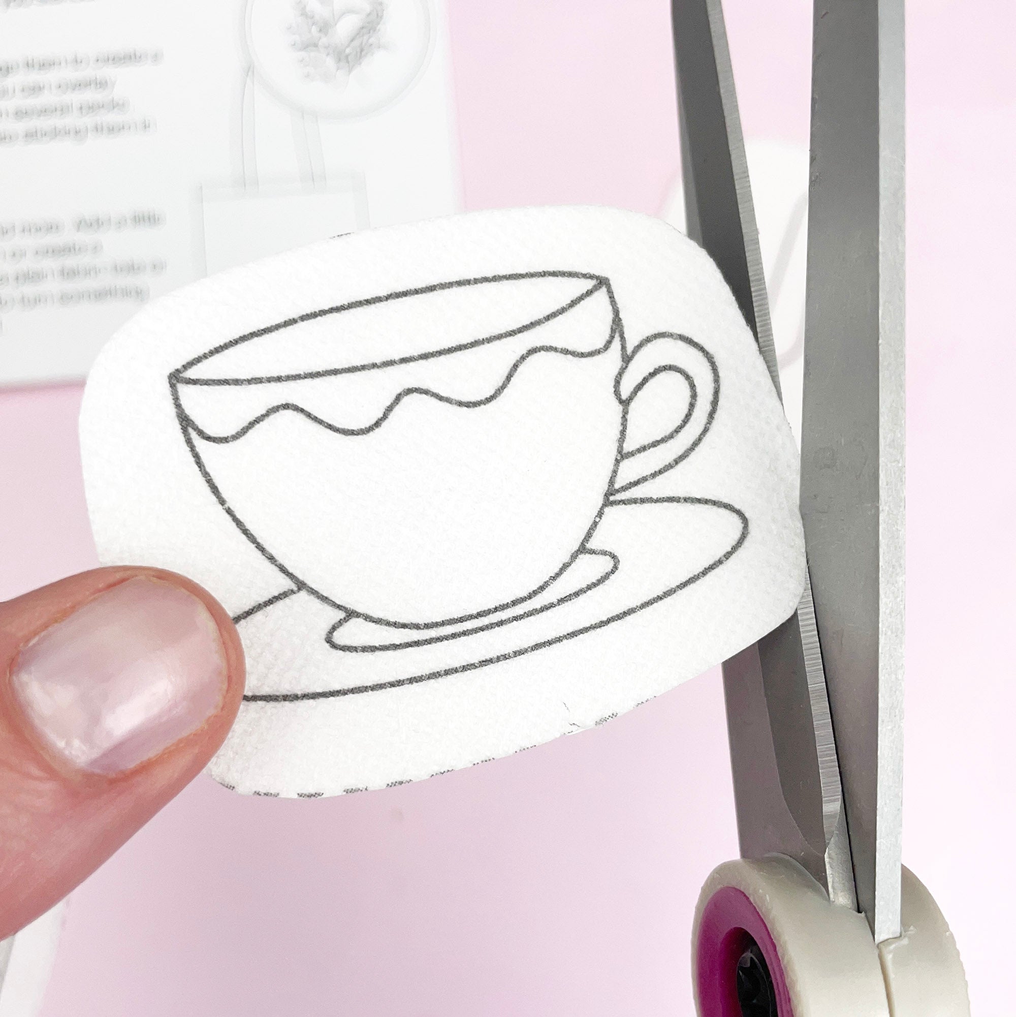 Hand cutting a fabric piece with printed tea cup embroidery pattern, beginner-friendly craft project.
