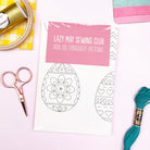 Iron on embroidery patterns from Lazy May Sewing Club with sewing tools on a white background