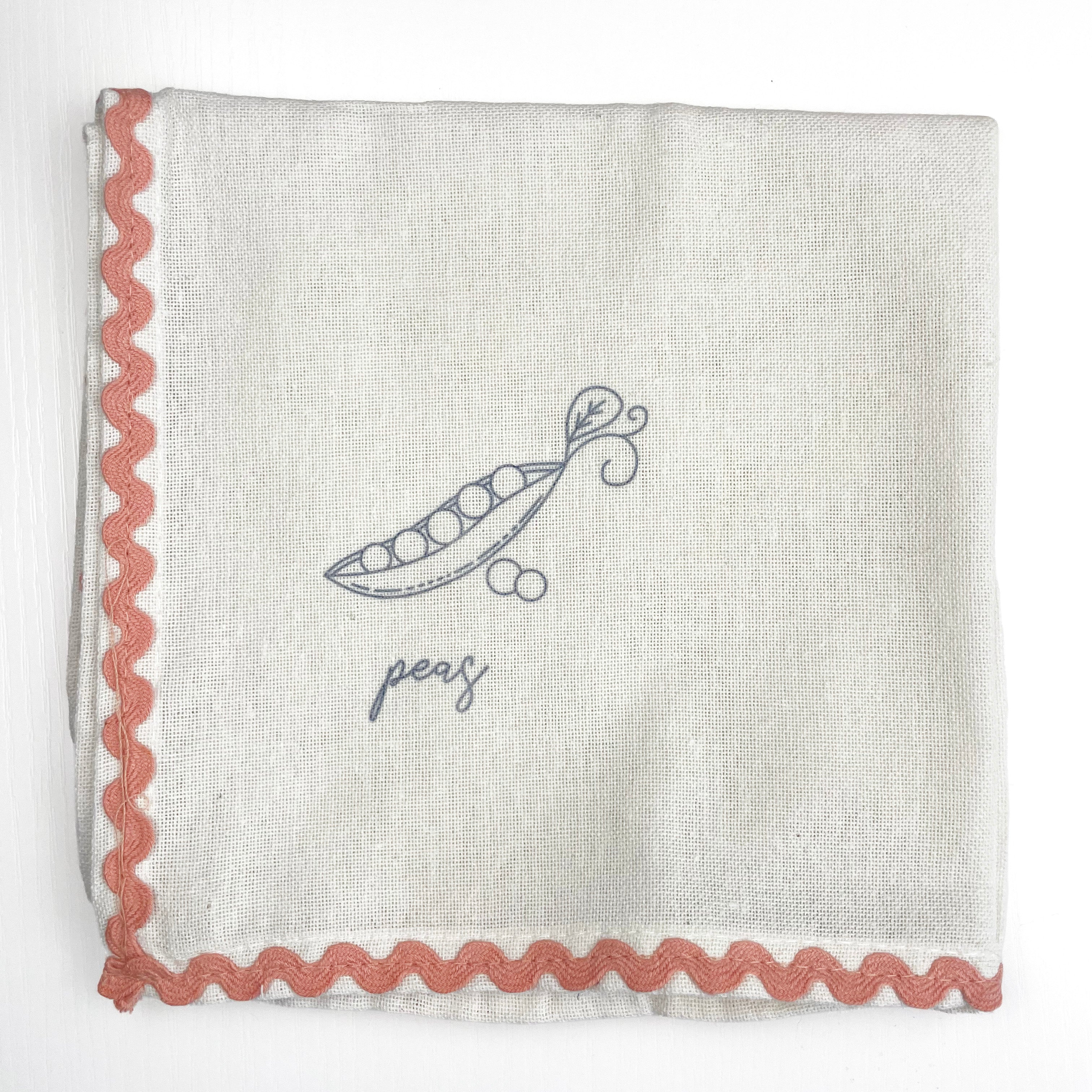 Fabric with embroidered design of a pea pod and the word 'peas' on a white background.