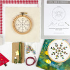 Embroidery hoop with snowflake design, embroidery book, and materials on a checkered fabric background.
