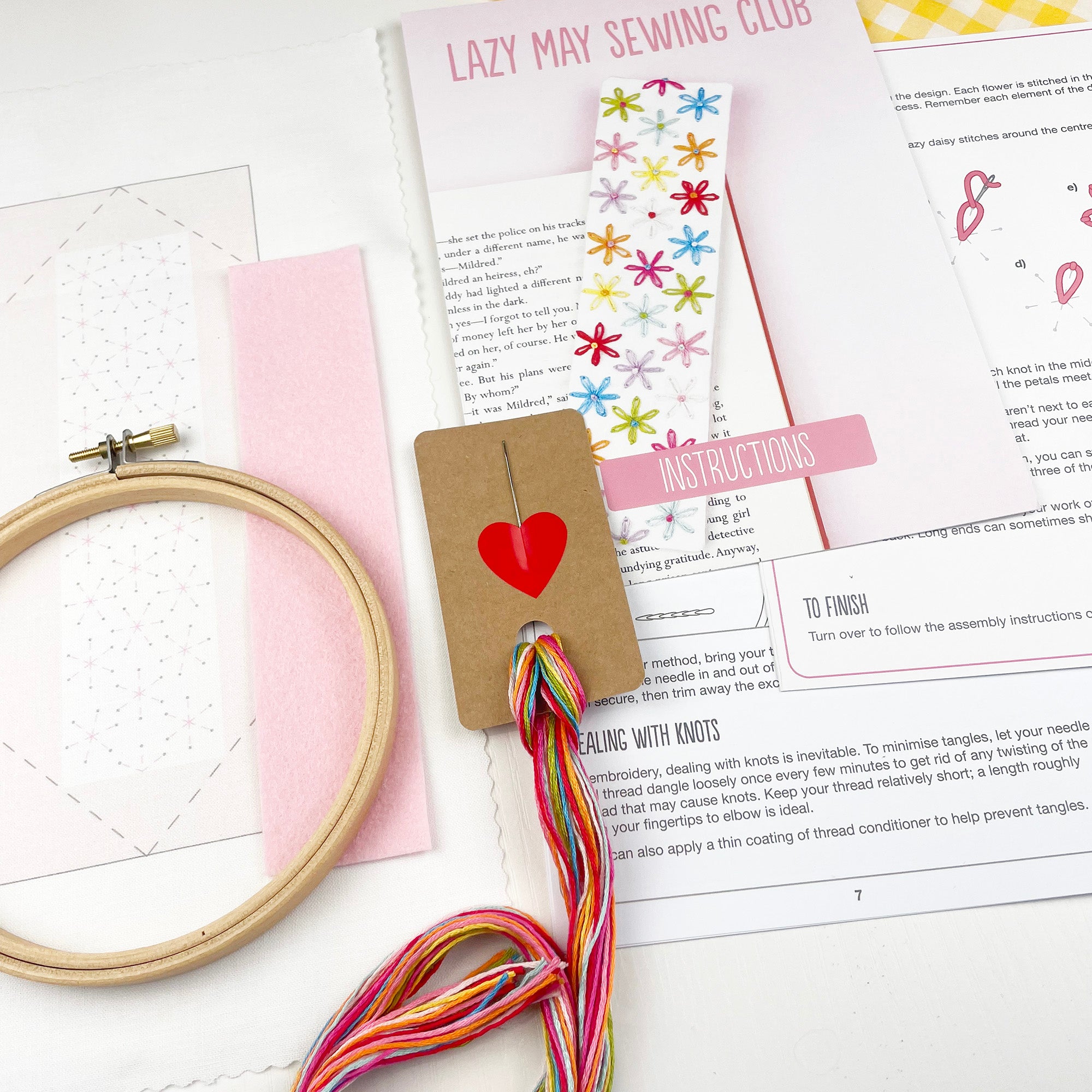 Embroidery hoop, colorful thread, and sewing club materials on a white surface