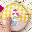 hands embroidering a hoop with a flower vase design