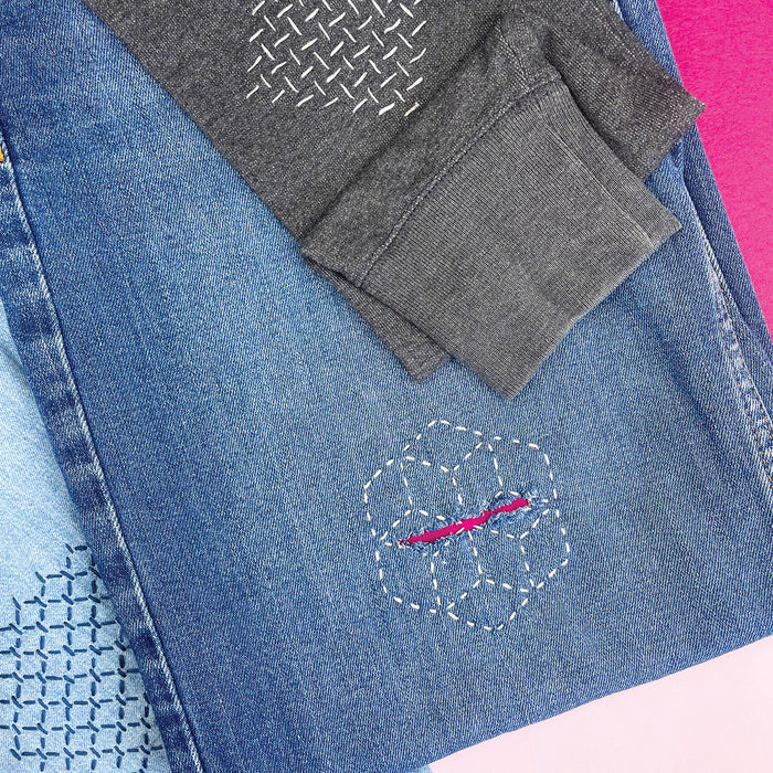 Examples of visible mending on denim and dark fabric using white and blue running stitches.