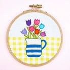 Embroidery hoop with colorful tulips and a striped pitcher on a yellow and white checkered background.