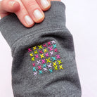 Hand-stitched colorful embroidery crosses on gray fabric showcasing Slow Stitching Textures: Stick and Stitch Embroidery Patterns.
