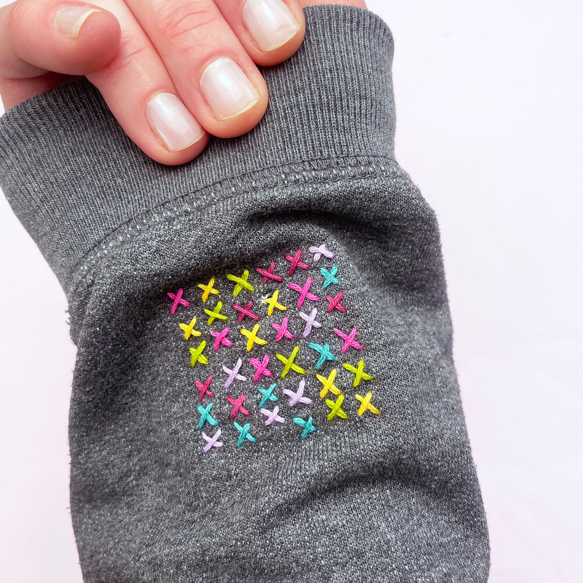 Hand-stitched colorful embroidery crosses on gray fabric showcasing Slow Stitching Textures: Stick and Stitch Embroidery Patterns.