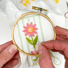 Person embroiderying a pink flower on green fabric with an embroidery hoop.