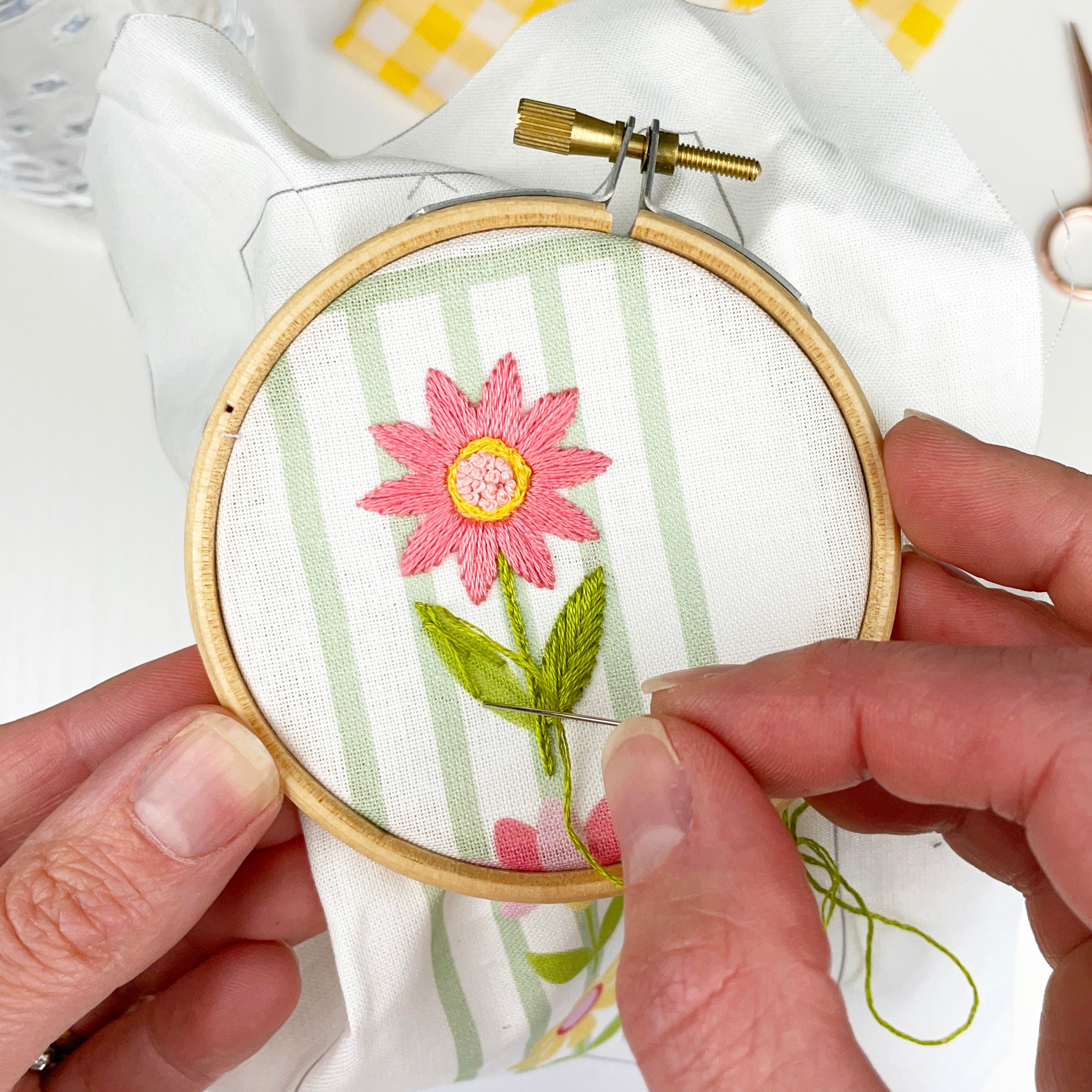 Person embroiderying a pink flower on green fabric with an embroidery hoop.