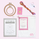 Embroidery kit contents including hoops, colorful threads, needle pack, stitch guide, and storage bag on a light background