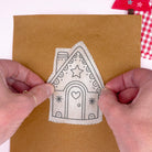 Hand holding a gingerbread house-embroidery stick and stitch pattern stuck on brown felt