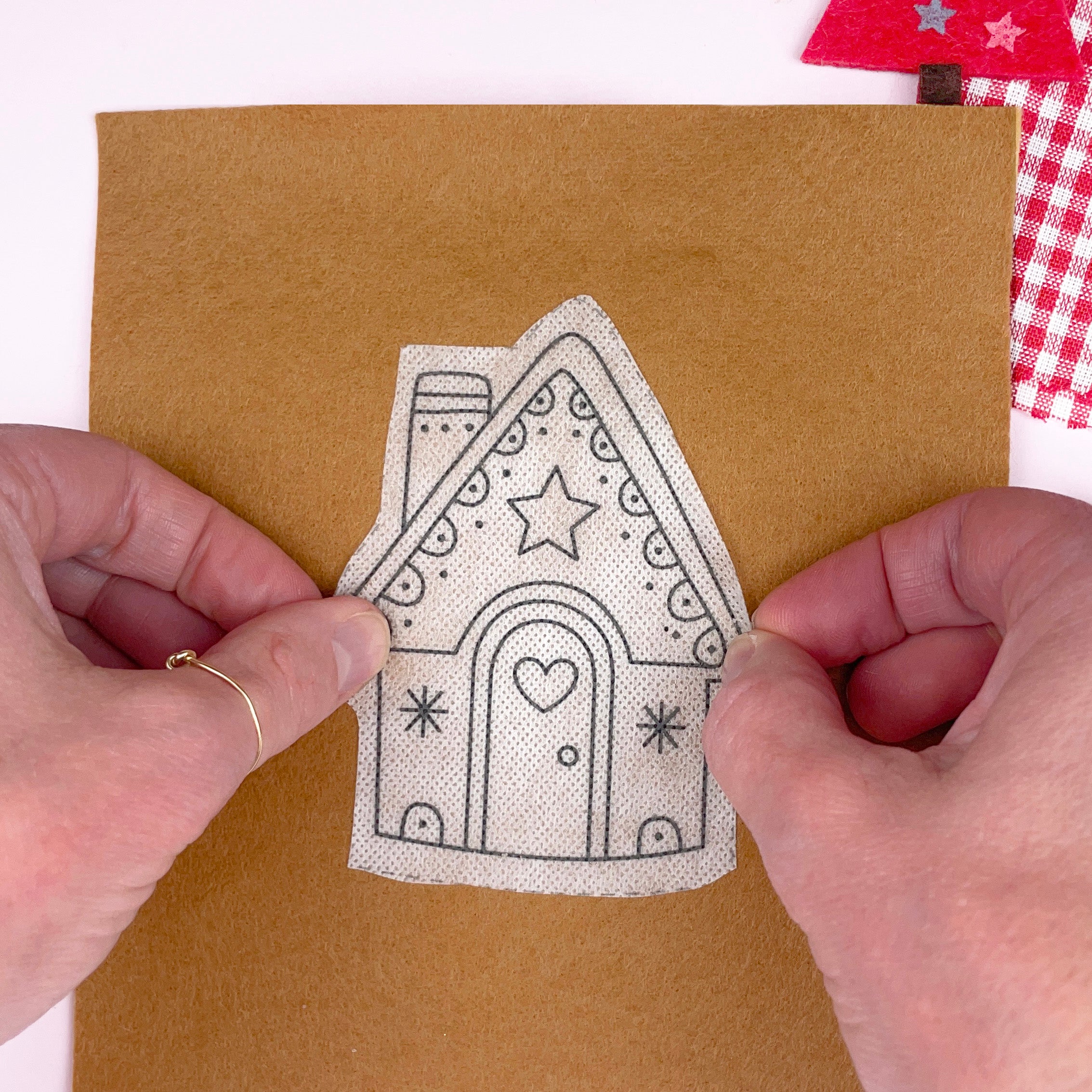 Hand holding a gingerbread house-embroidery stick and stitch pattern stuck on brown felt