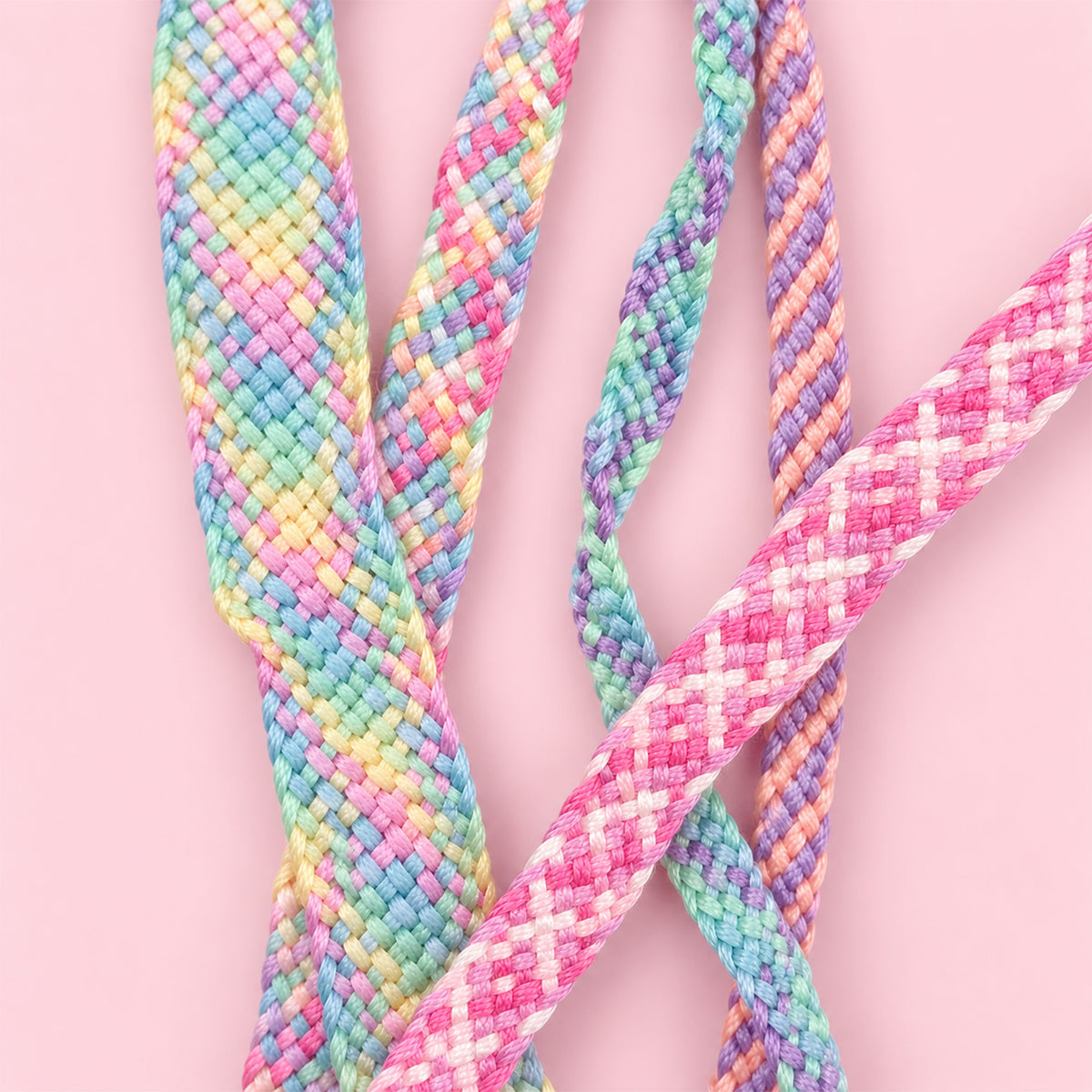 Close-up of four braided rope cords in pastel rainbow colors, including pink, blue, green, yellow, and purple, arranged on a solid light pink background.