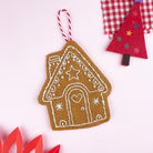 Felt gingerbread house ornament with a tree and star on a light pink background