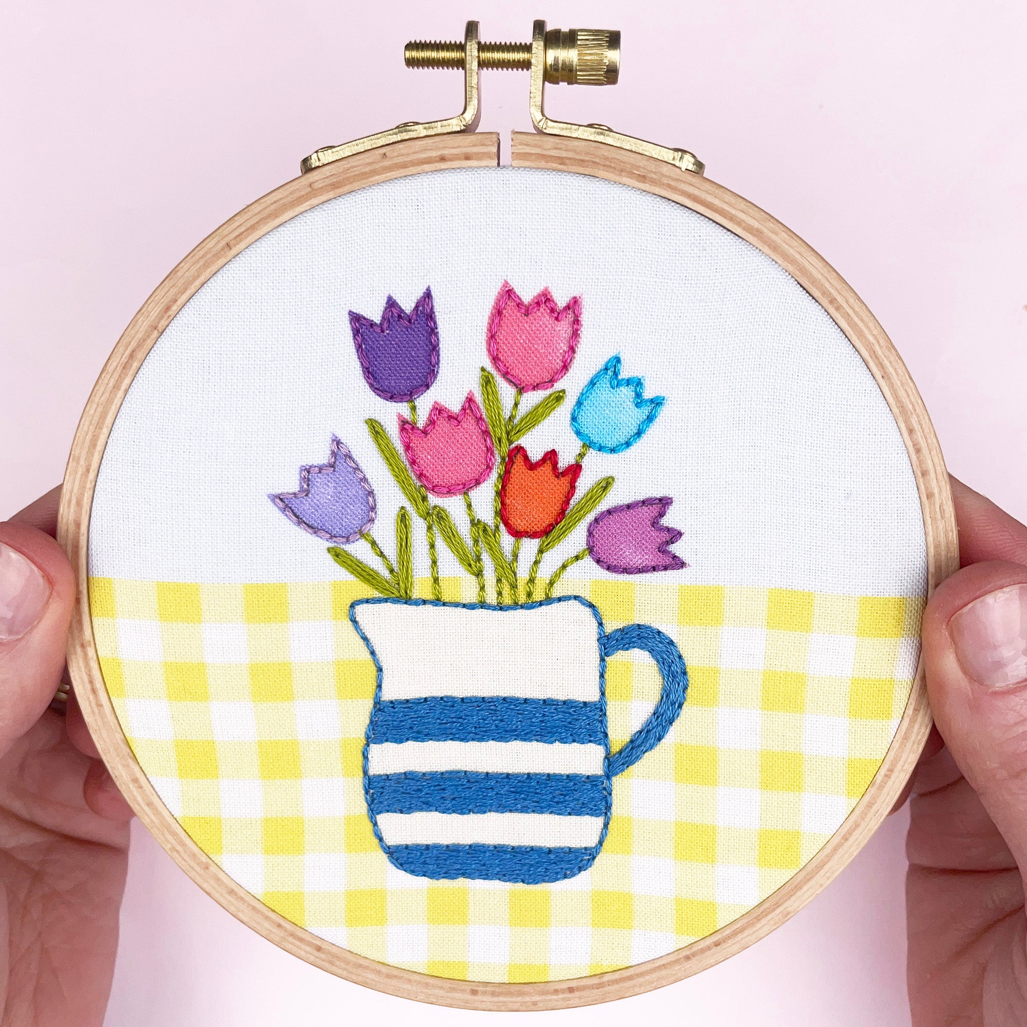 Embroidery hoop with colorful tulips and a striped mug on a checkered background