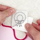 Person holding a small embroidered patch with a design of a wreath and bow.
