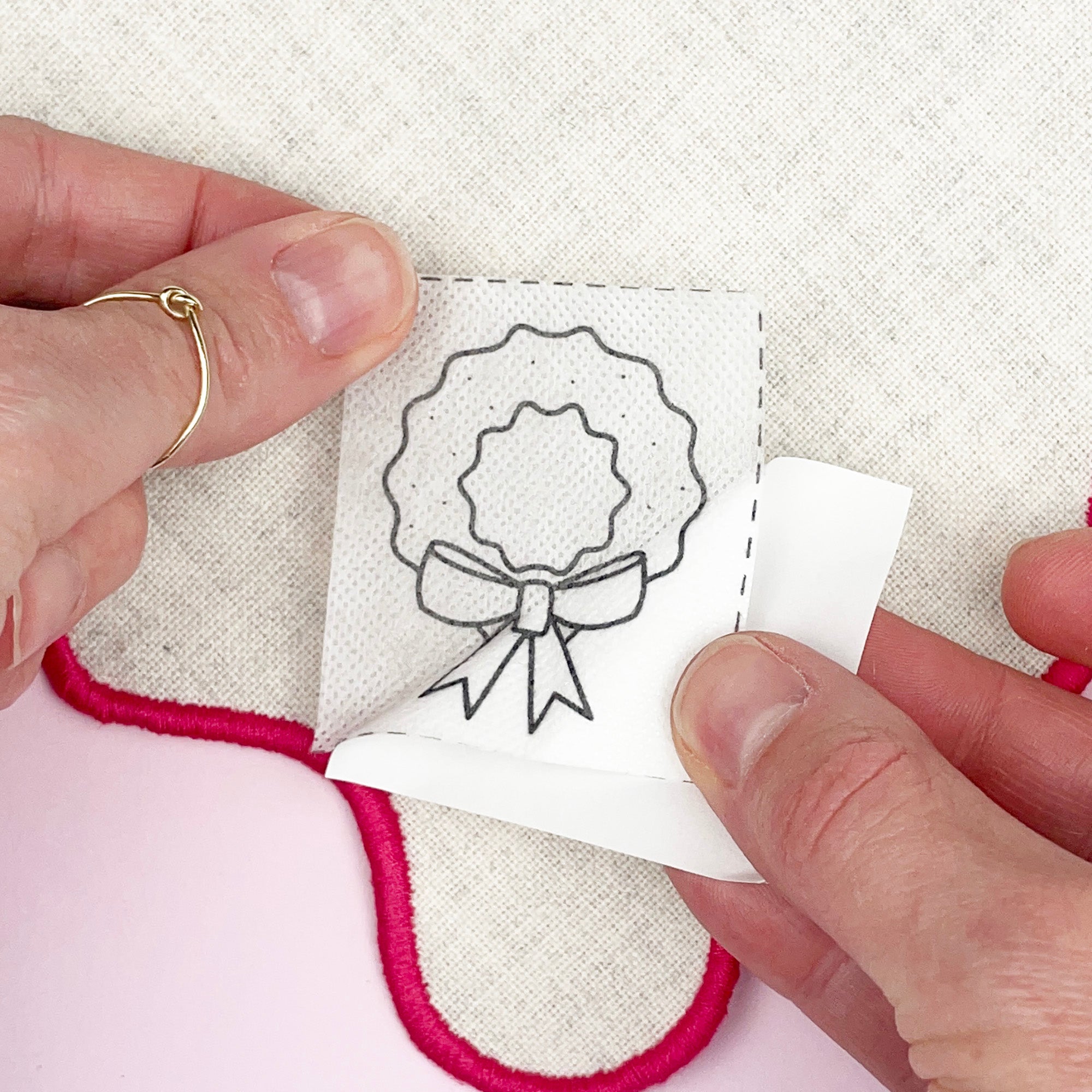 Person holding a small embroidered patch with a design of a wreath and bow.