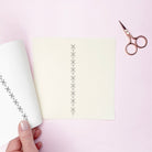 Hand holding an iron on embroidery pattern with decorative cut-out patterns on a pink background with scissors. Ironed on to fabric