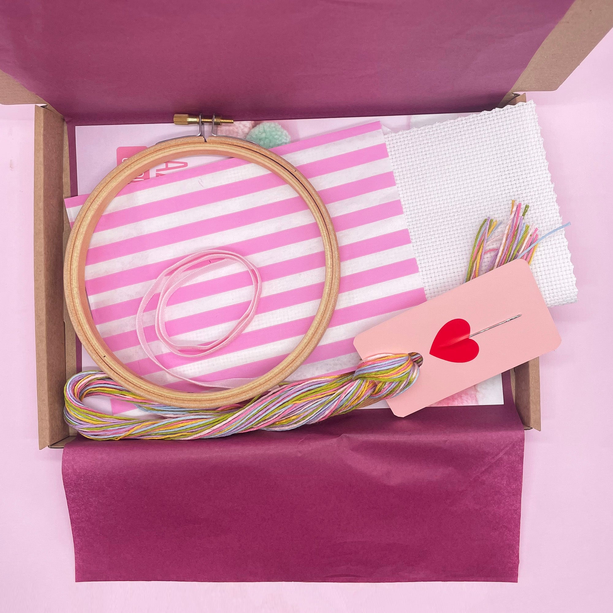 The cross-stitch kit components neatly arranged, including the embroidery hoop, fabric, thread, needle, and instruction booklet. Each item is organized to showcase the complete set provided for beginners.