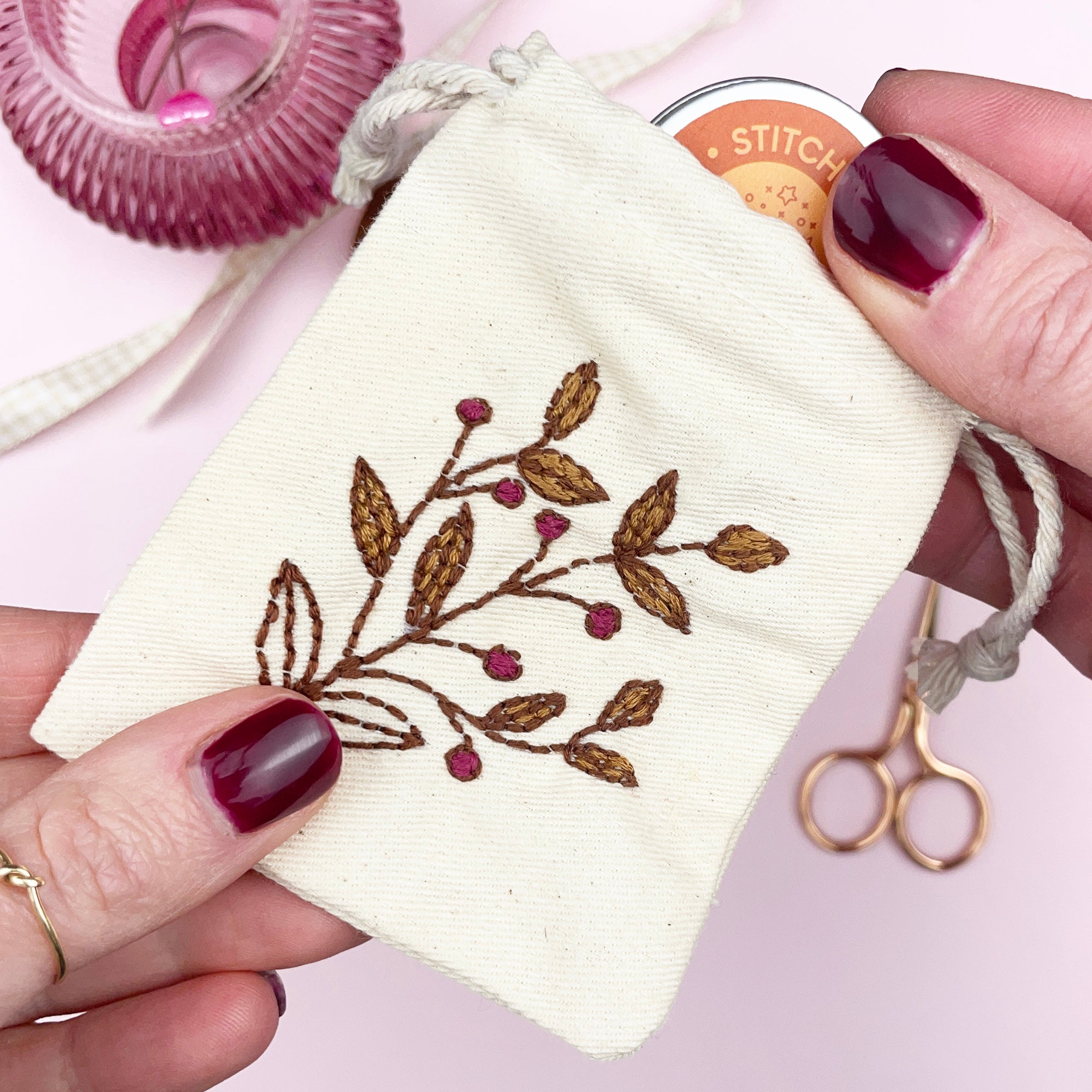 Hand holding a small embroidered pouch with floral design on a pink background