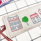 Embroidered fabric with houses and a tree on a checkered background