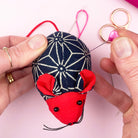 Small mouse-shaped sewing pin cushion in patterned navy fabric with red details, used for holding needles.
