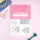 Package of Little Houses: Stick and Stitch Embroidery Patterns with scissors, thread, and embroidery hoop on pink background