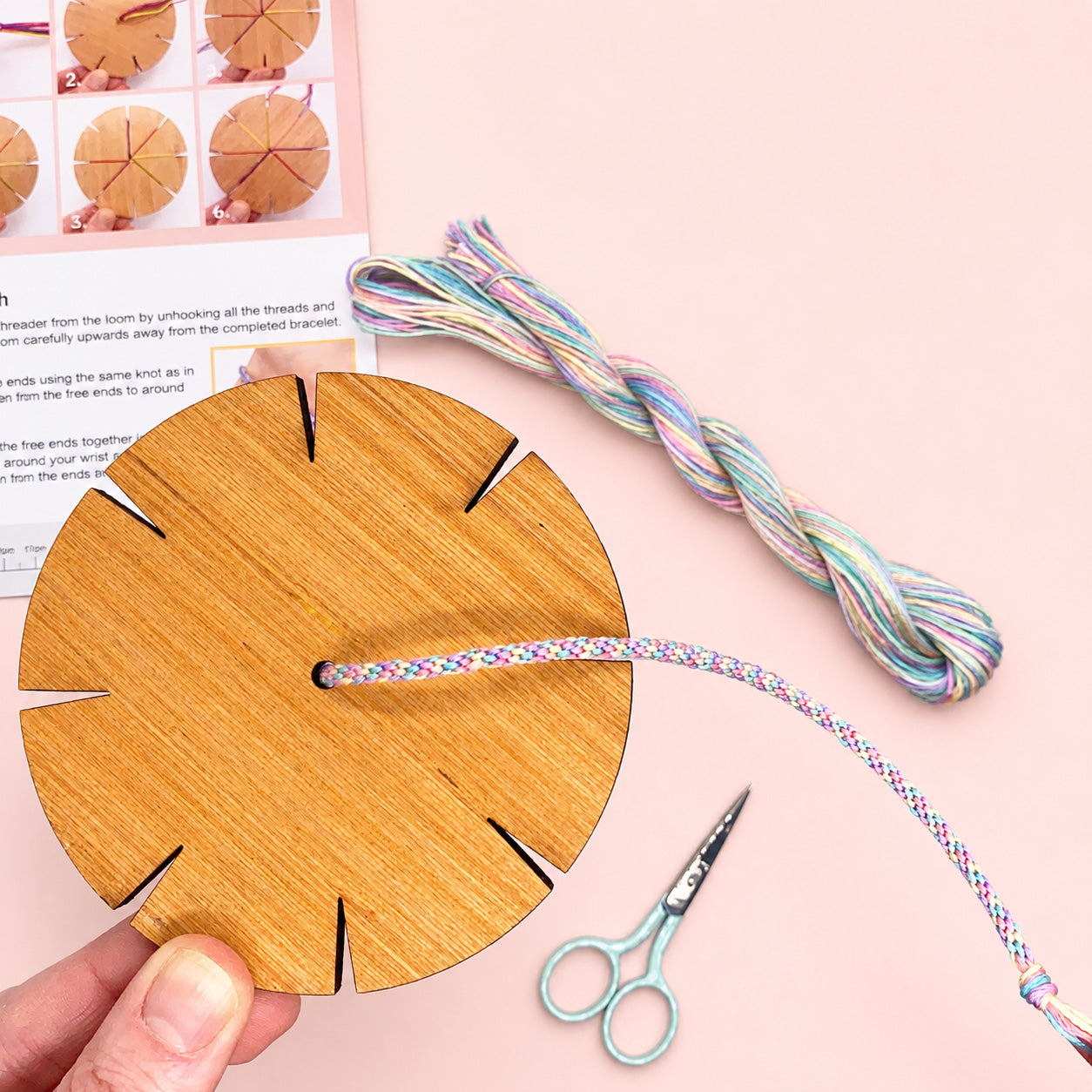 Wooden loom with colorful yarn and scissors on a pink background