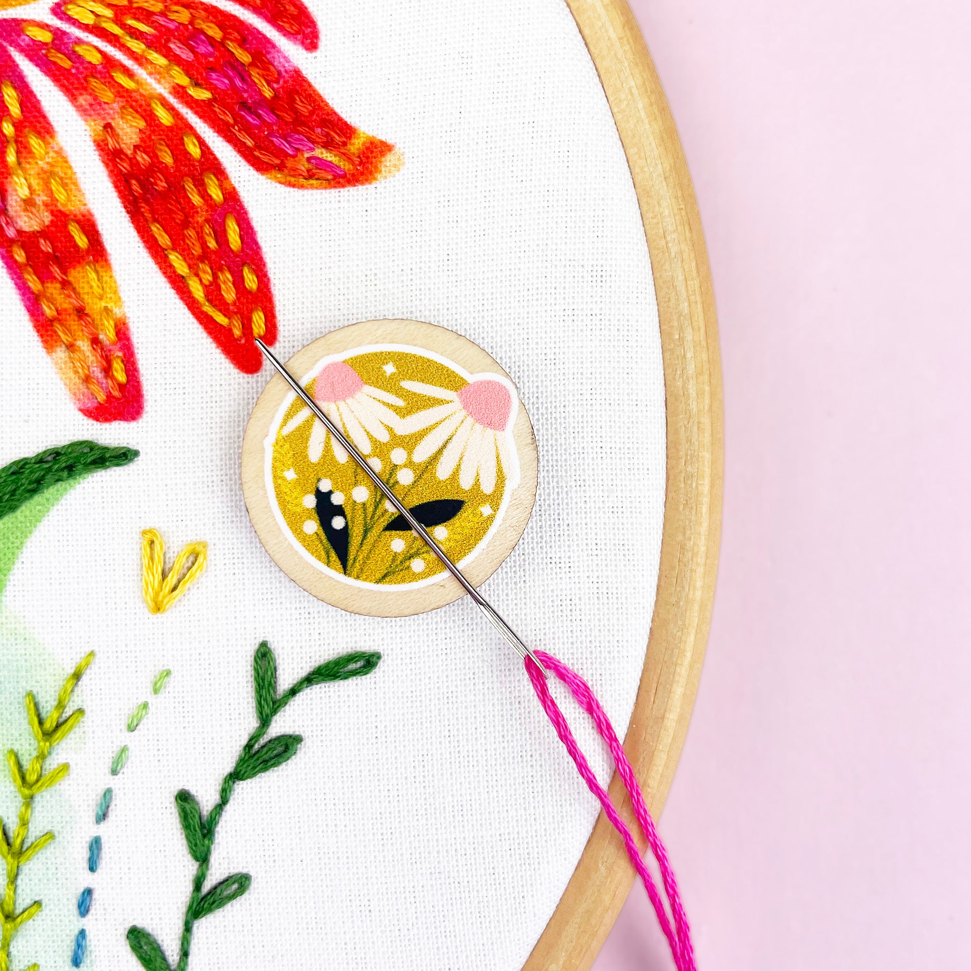 Embroidery hoop with floral design and wooden needle minder on a pink background