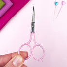 Pink-handled scissors held by a hand on a pink background