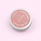 Thread conditioner container with pink lid and silver base on a light pink background