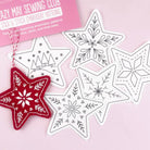 Six star-shaped embroidery pattern pieces with snowflake and tree designs are arranged on a light pink background, with a pink package card reading 'Lazy May Sewing Club Stick & Stitch Embroidery Patterns' and a red embroidered star ornament hanging from one piece.