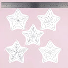 Five white star-shaped embroidery  templates or patterns with black line-art holiday designs, arranged on a light pink background with a metal ruler at the top for scale.