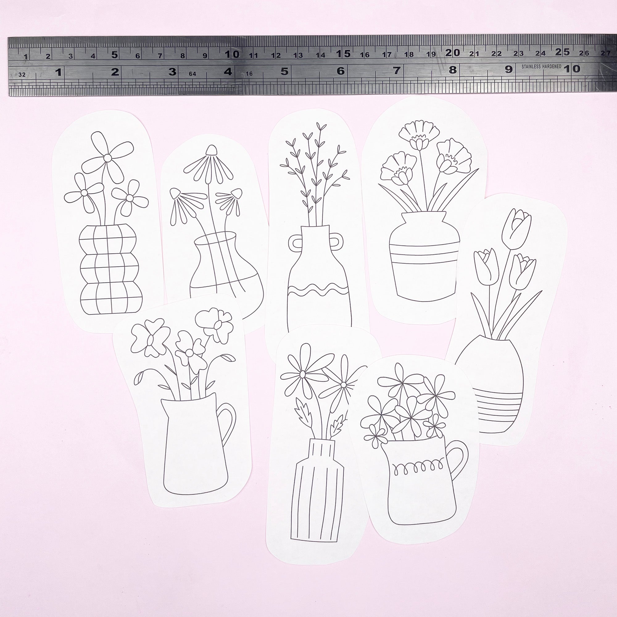 Set of floral and vase embroidery patterns with a ruler for scale on a light pink background