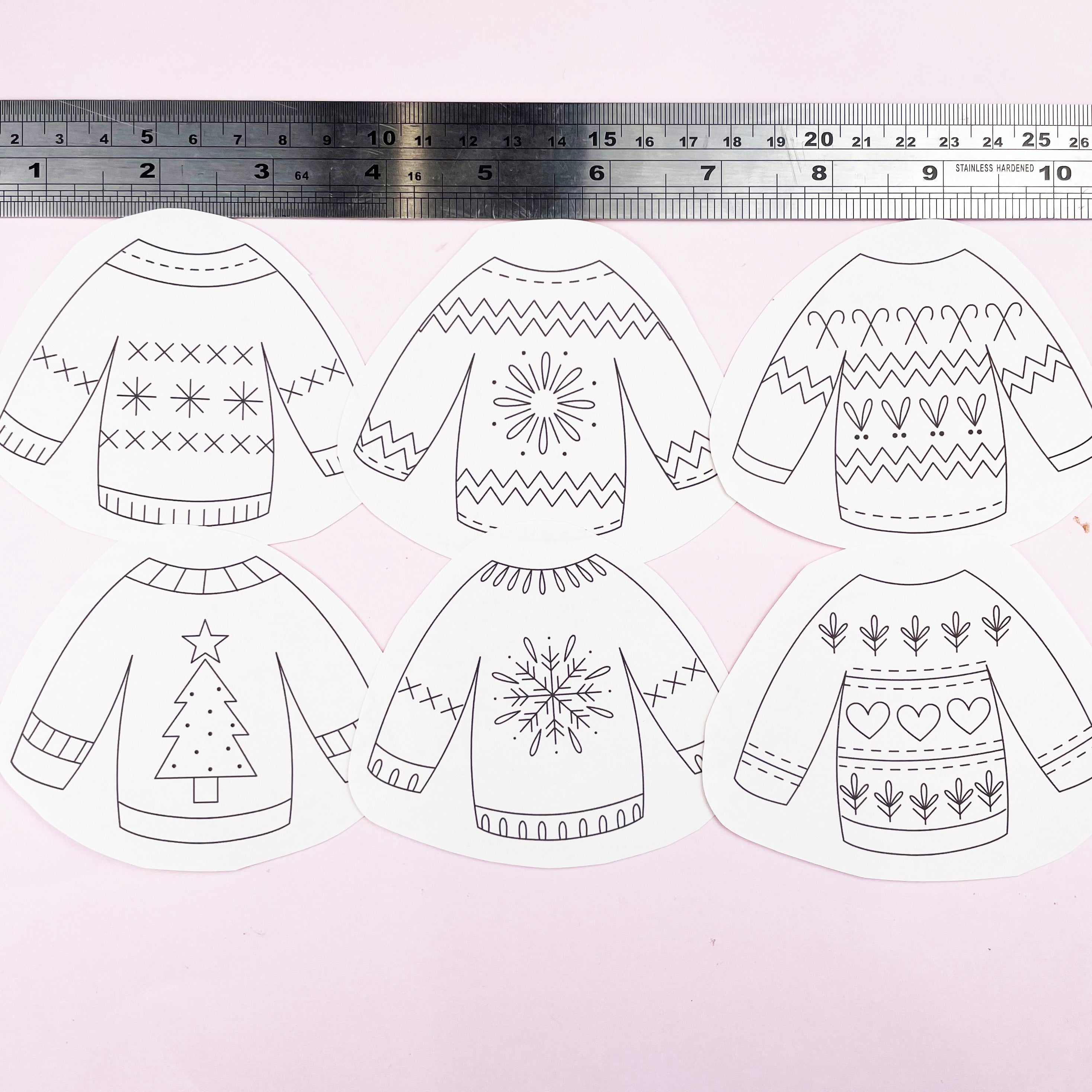 Set of six black and white sweaters embroidery pattern designs with patterns on a light pink background, accompanied by a ruler for scale.