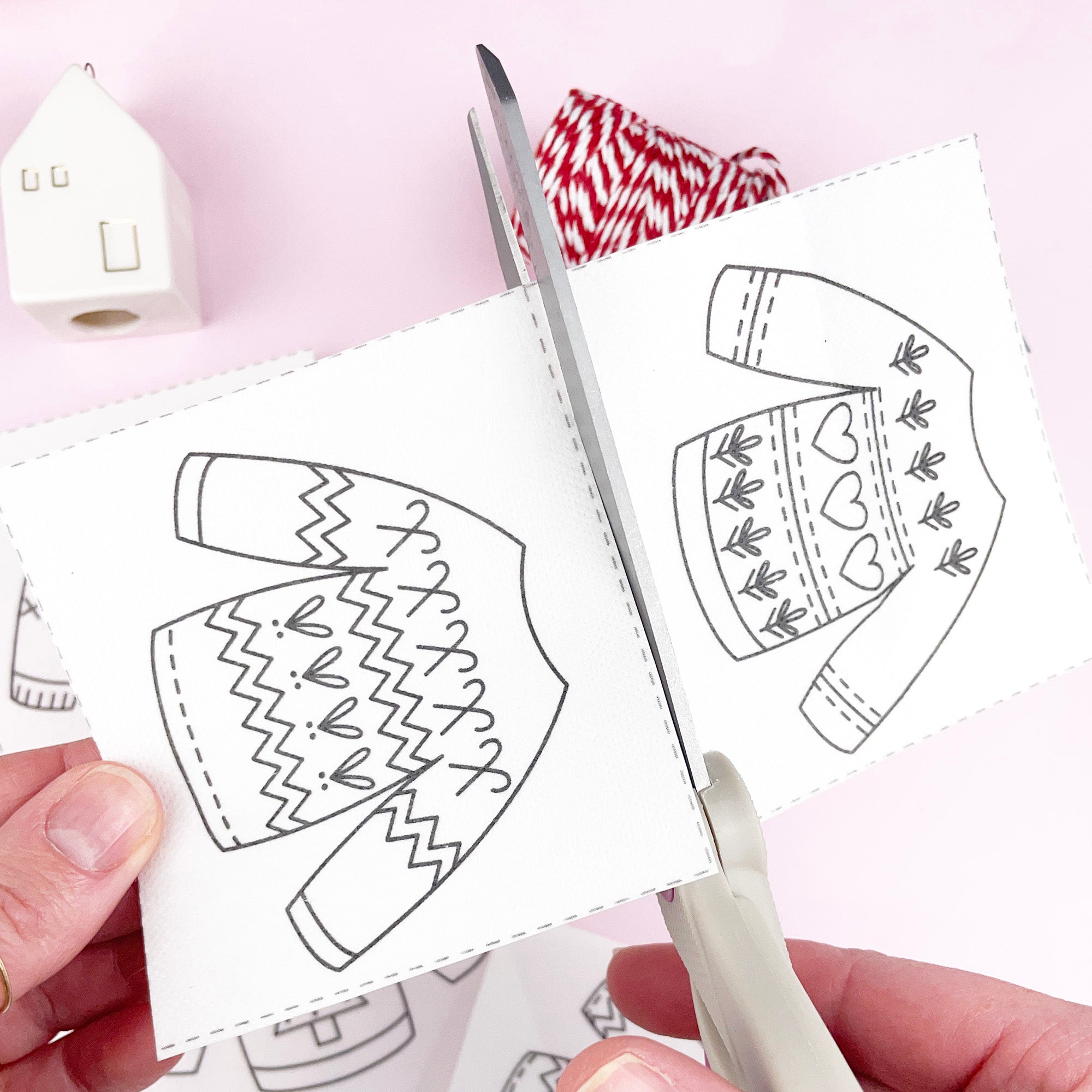 Hands holding an embroidery pattern with jumper / sweater designs and scissors on a pink background